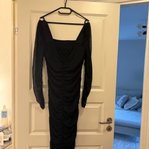 Svart långklänning med meshärmar - Elegant svart långklänning med långa meshärmar och rynkad design. 