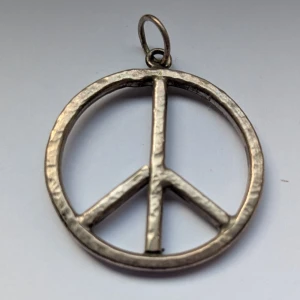 Silverfärgad peace-symbol - Snygg och stilren peace-symbol i silverfärg. Perfekt för att ge din outfit en touch av retro och fredlig stil. Hängsmycket är runt och har en enkel ögla för kedjan.