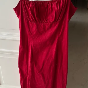 Röd klänning med smala axelband - Snygg röd klänning med smala axelband och elastisk överdel. Perfekt för en somrig look. Klänningen har en enkel design som gör den lätt att matcha med olika accessoarer.