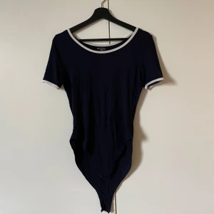 Mörkblå bodysuit från Brave Soul - Säljer en mörkblå bodysuit från Brave Soul med vita kanter. Den har korta ärmar och en rund halsringning. Storlek S. Använd flera gånger men i bra skick. Bra att veta: hund finns i hemmet 🐶
