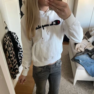 Vit hoodie från Champion - Säljer en vit hoodie från Champion med deras ikoniska logga broderad på framsidan. Tröjan har en klassisk känguruficka och justerbar huva med snören. Perfekt för en avslappnad stil. Liten fläck längst ned (sista bilden)💕