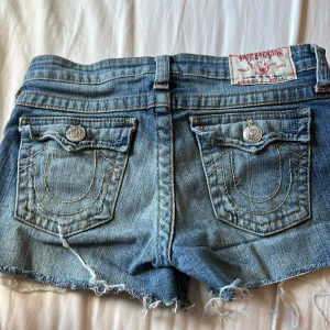 Blå jeansshorts från True Religion - Säljer ett par snygga blå jeansshorts från True Religion. De har fransiga kanter och klassiska fickor med knappar bak. Midjemått är ca 35 cm. Priset kan diskuteras vid en snabb affär. Skriv innan ni köper.💗