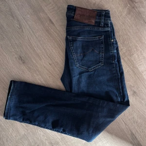 Jacob Cohen Jeans - Snygga mörkblå jeans från Jacob Cohen med klassisk femficksdesign och knappgylf. Tillverkade i Italien med högkvalitativt denim. Perfekta för en stilren look. Jeansmodellen heter nick och sitter slimfit.