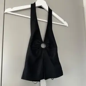 Snygg svart halterneck topp med glittrigt tyg och en unik ringdetalj framtill. Perfekt för en utekväll eller fest. Toppen har en djup urringning och slit i fram. Aldrig använd, prislapp är kvar. Nypris 99