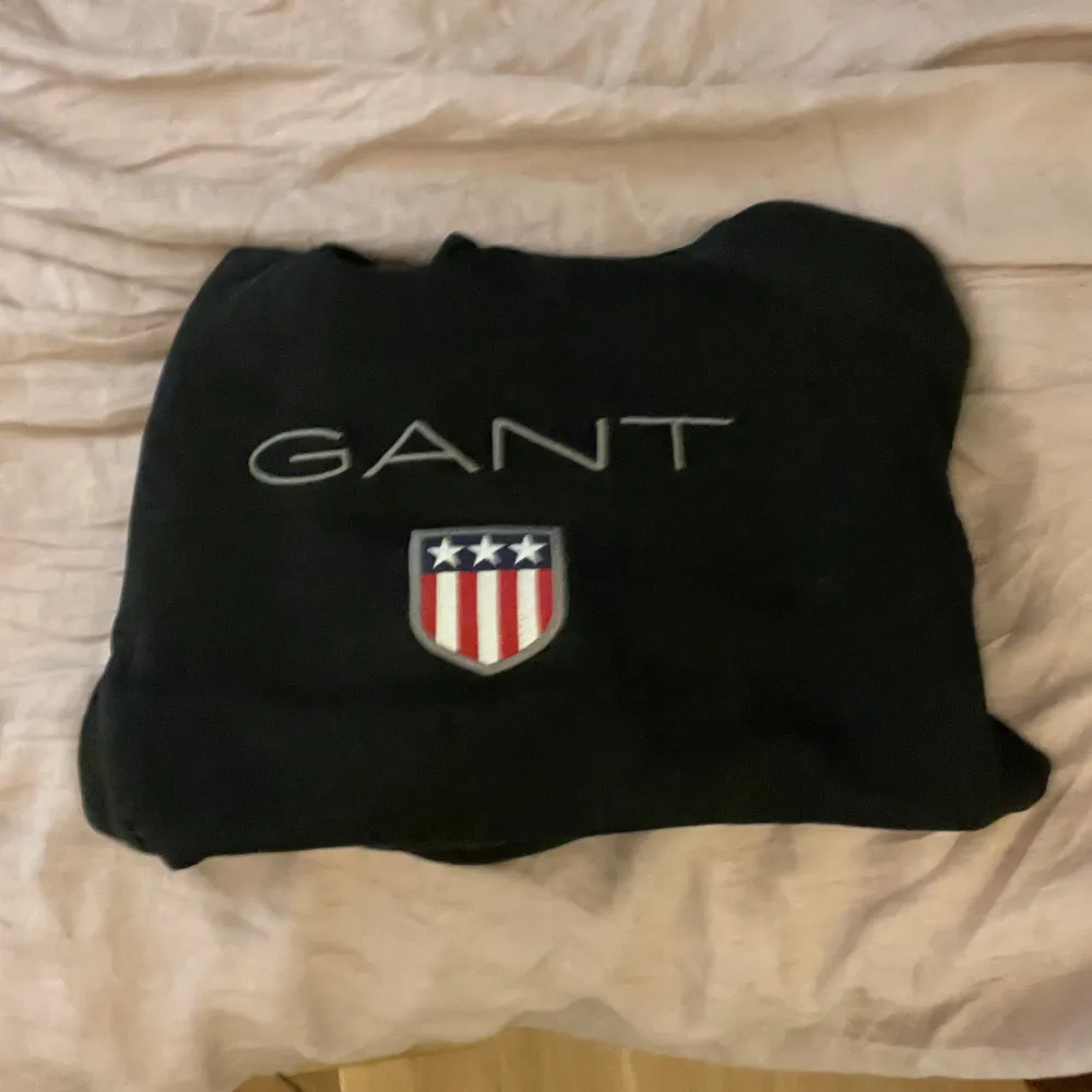 Säljer en svart hoodie från GANT med ett broderat emblem på bröstet. Tröjan har en klassisk design med huva och en stor ficka framtill. Perfekt för en avslappnad stil. Den är helt ny köpte den igår. Neuletakit & Villapaidat.