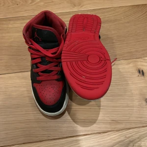 Nike Air Jordans i svart och rött - Säljer ett par äkta klassiska Nike Air Jordans i svart och rött. Skorna har en hög design med snörning och den ikoniska Nike-loggan på sidan. Perfekta för dig som vill ha en stilren och sportig look.