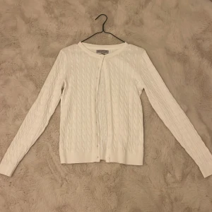 Vit kabelstickad kofta från Basic You - Säljer en stilren vit kabelstickad kofta från Basic You i ekologisk bomull. Koftan har långa ärmar och knäppning framtill, perfekt för en klassisk look. Passar bra till både jeans och kjol. 🌟