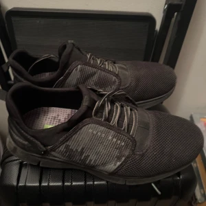 Svarta sneakers från Hugo Boss - Snygga svarta sneakers från Hugo Boss med ett diskret mönster på sidan. Skorna har snörning och en bekväm sula, perfekt för vardagsbruk. De har en modern design med en touch av stilren elegans.