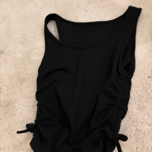 Svart ribbad topp - Snygg svart topp med ribbad textur och knytning på sidan. Perfekt för en stilren look. Passar bra till både jeans och kjol.