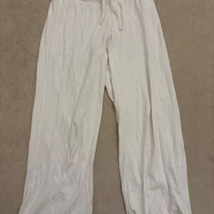 Vita byxor med snörning - Snygga somriga vita byxor med snörning i midjan. Byxorna har ett diskret randigt mönster och är tillverkade i ett mjukt material som ger en bekväm passform. Perfekta för en avslappnad stil. 