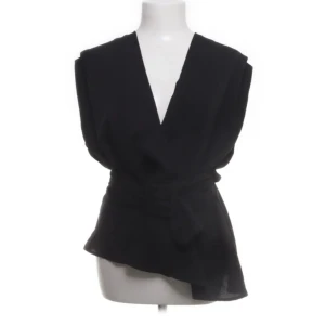 Svart omlottopp med knyt - Elegant svart omlottopp med knyt i midjan. Toppen har en v-ringad design och är ärmlös, vilket ger en stilren och modern look. Perfekt för att skapa en chic outfit. Skriv om fler bilder !