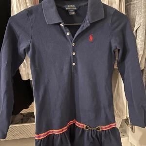 Marinblå klänning från Polo Ralph Lauren - Säljer en stilren marinblå klänning från Polo Ralph Lauren med klassisk krage och knappar där fram. OBS! Ska även till lägga att klänningen är i storlek s för barn!! 