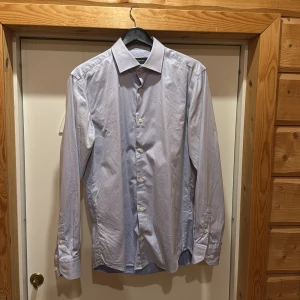 Ljusblå skjorta från Dressmann - Snygg ljusblå skjorta från Dressmann i premium bomull. Skjortan har en klassisk krage och knappar framtill. Perfekt för en stilren look. 