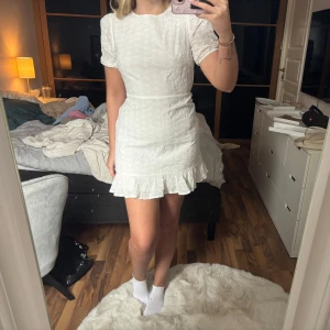 Vit klänning från NA-KD - Säljer en söt vit klänning från NA-KD med korta ärmar och volangdetaljer. Klänningen har en öppen rygg och ett fint broderat mönster. Perfekt för sommarens alla tillfällen! 🌸Klänningen har en ytterst liten sminkrand runt halsen, men inget som syns värst mycket! 