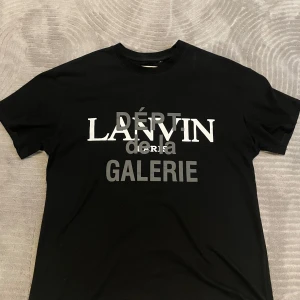 Svart Lanvin x Gallery Dept t-shirt - Snygg svart t-shirt från Gallery Dept. i samarbete med Lanvin. Stor tryckt logga framtill med texten 'DÉPT de la GALERIE LANVIN PARIS' och en stor G-logga på ryggen. Klassisk passform och rund hals. Den sitter med en boxy fit. Perfekt för dig som gillar streetwear och statement-plagg. S men passar mer som M. Använd 1 gång. Vet inte om den är äkta