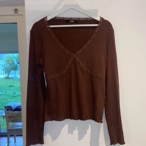 Brun ribbad topp med spets från BikBok - Säljer en brun långärmad topp från BikBok i ribbat material. Toppen har v-ringning och spetsdetaljer.