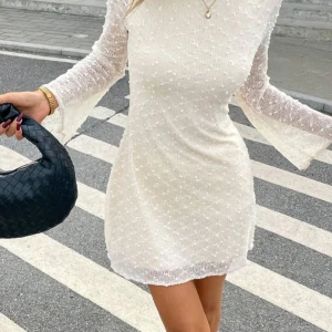 Vit kortklänning med vida ärmar  - Superfin vit kortklänning med diskret prickigt mönster och transparenta volangärmar. Klänningen har en figurnära passform materialet känns lätt och luftigt.