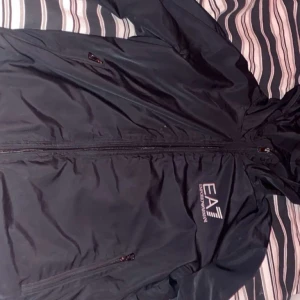 Svart vindjacka från EA7 Emporio Armani - Superlätt och stilren jacka, perfekt för vår/sommar. Pris: 400 kr eller bud. Kan skickas eller mötas i vingåker/katrineholm bytt dragkedja annars är allt som normalt 