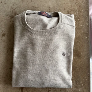 Beigefärgad merinoullströja Morris - Snygg beige stickad tröja från Morris i 100% merinoull. Klassisk rund halsringning och diskret broderad logga på bröstet. Perfekt för lager-på-lager och passar till allt. Enkel och stilren design med lång ärm.