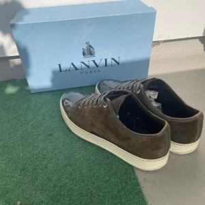Lanvin sneakers i mocka och lack - OBS! Dessa är olivgröna. Snygga sneakers från Lanvin i mörkgröna mocka med svart lackad tå och vita sulor. Skorna har klassisk snörning och en stilren, rund tå. Perfekta för dig som gillar lyxiga detaljer och en unik mix av material. Skorna är i UK9. Vid frågor och funderingar är det bara att höra av sig.
