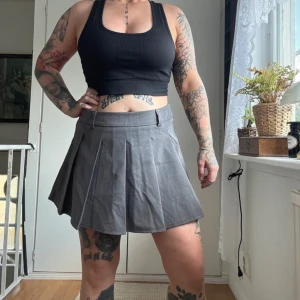 Grå plisserad kortkjol med inbyggda shorts  - Säljer en snygg grå plisserad kortkjol med bälteshällor i midjan. Kjolen har en klassisk A-linjeform och är perfekt för dig som gillar en stilren och trendig look. Passar till crop tops och chunky sneakers.