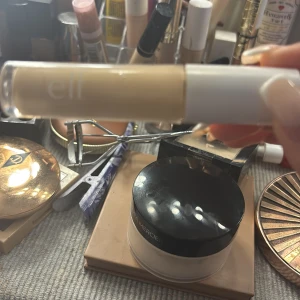 e.l.f. concealer i ljus nyans - Concealer från e.l.f. i en ljus beige ton, perfekt för att täcka mörka ringar och ojämnheter. Kommer i en smidig tub med vit applikator. Passar dig som vill ha en naturlig och fräsch look.