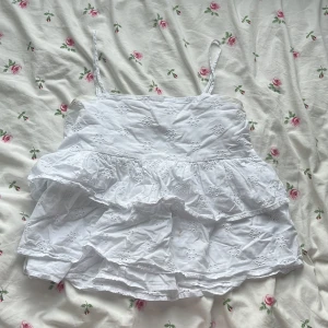 Vit volangtop från Gina Tricot - Supersöt vit linnetopp från Gina Tricot med broderade blommor och volangdetaljer. 