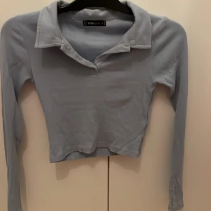 Ljusblå pikétröja  - Säljer en ljusblå pikétröja i storlek S. Tröjan är croppad med lång ärm och klassisk krage. Perfekt för dig som gillar en stilren och trendig look. Materialet är mjukt och stretchigt för en bekväm passform. Aldrig använd 🩵