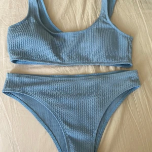 Ljusblå ribbad bikini - Superfin ljusblå bikini med ribbad struktur. Toppen har breda axelband och sportig form, medan bikinitrosan har en klassisk midja. Bortklippta lappar men skulle tippa på storlek S i både topp och nederdel! Skriv för mer info!