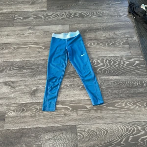 Nike Pro blå leggings Dri-FIT - Säljer ett par blå Nike Pro leggings med Dri-FIT-teknologi. De har en bred resår i midjan med Nike Pro-tryck och en tight passform som sitter snyggt på kroppen. Perfekta för träning eller sport. Swoosh-logga på benet för extra stil.