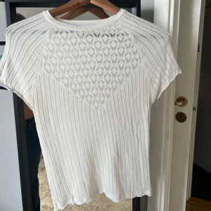 Vit stickad kortärmad tröja - Superfin vit stickad tröja med korta ärmar och snyggt hålmönster över hela plagget. Tröjan har rund halsringnin!