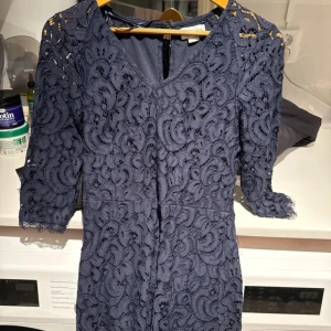 Marinblå spetsklänning - Supersnygg marinblå kortklänning  med v-ringning och trekvartsärm. Klänningen är helt täckt av vacker spets och har en figurnära passform. 