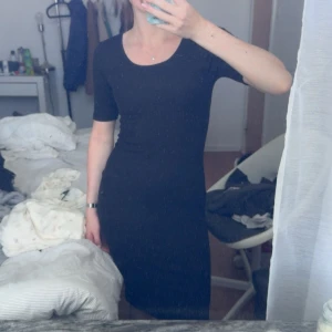 Svart tight klänning med kort ärm - En svart, figurnära klänning med rund halsringning och korta ärmar. Enkel och stilren design som passar perfekt för dig som gillar minimalistiskt mode. Klänningen har en smickrande passform och slutar strax ovanför knäna.