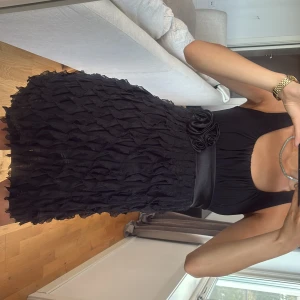 Svart kort klänning med volangkjol - Supersöt svart kort klänning med volangkjol och markerad midja med bredt satinband och rosettdetalj. Rosett bakom ryggen. 