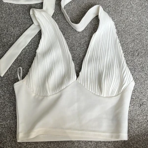 Vit omlott halterneck topp - Snygg vit omlott topp med djup v-ringning och breda knytband i nacken. 