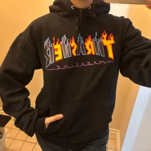  Thrasher limited edition  - Svart hoodie från Thrasher med ikoniskt flame-tryck i gult, rött och blått på bröstet. Klassisk känguruficka, huva med snörning och mjukt material. Perfekt för dig som gillar streetwear och vill sticka ut med färgglad logga. Denna modell på hoodien är av begränsad upplaga och finns inte att köpa längre. 