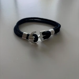 Marinblått armband med silverfärgad ankare - Stilrent armband med marinblått rep och en silverfärgad ankardetalj som lås. Detaljer i vitt runt ankaret ger en marin känsla. Perfekt accessoar för dig som gillar enkel men snygg design.
