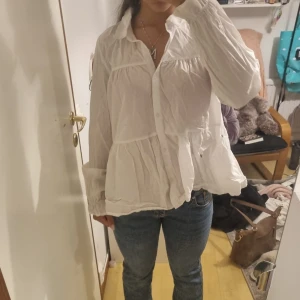 Vit volangskjorta med knappar - Säljer en luftig vit skjorta med volanger och långa puffärmar. Skjortan har knappar framtill och en lös passform som ger en avslappnad och trendig look. Perfekt att styla med jeans eller kjol för en chill vibe.