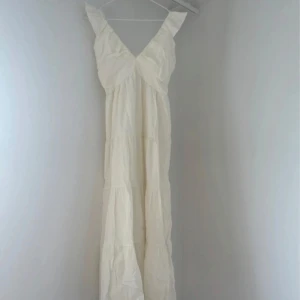 Vit långklänning med volangärmar - Luftig och romantisk vit långklänning med v-ringning och breda volangärmar. Smockad rygg,Perfekt för sommarens alla tillfällen.