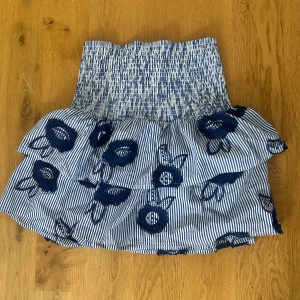 Randig volangkjol - Kort volangkjol från Holly & Whyte med blåvita ränder och broderade blommor. 