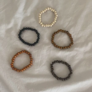 Fem armband med träpärlor - Två elastiska armband med runda träpärlor, ett i mörkbrunt och ett i svart, Ett i brun och ett i lite mer röd/orange de sista armbandet är i vitt. Perfekt accessoar för en chill och naturlig look. Säljs tillsammans! Eller styck. Styck pris är 39 kr tillsammans får du dem för 150. Köpta på nätet och har inget märke. Skriv om ni vill ha styck.