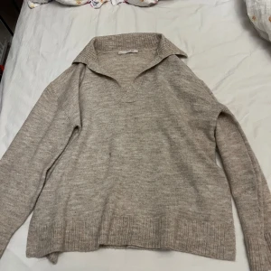 Beige stickad tröja med krage 157 - Beige stickad tröja från 157 med bred krage och v-ringning. Tröjan har lång ärm och ribbade muddar vid ärmslut och nederkant. Perfekt för lager-på-lager och chill höst- eller vinterstil. Har en fläck på sig som syns på bild 