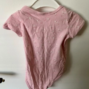 Rosa långärmad tröja LCW baby - Supersöt rosa långärmad tröja från LCW baby med trycket 'be happy everyday' och små blommor framtill. Tröjan har knapp vid axeln för enkel påklädning och är gjord i mjuk bomull. Perfekt för lek och chill dagar.