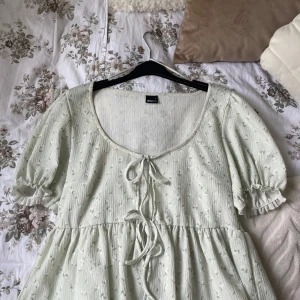 Ljusgrön blommig blus från Gina Tricot  - Supersöt ljusgrön blus från Gina Tricot i storlek L med små blommor, puffärmar och två knytband framtill. Den är luftig och passar perfekt till sommaren! Köptes ny i butik förra sommaren och använd fåtal gånger. 