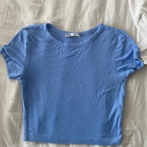 Blå croppad topp från Zara - En enkel och stilren ljusblå croppad topp från Zara. Modellen har korta ärmar och rund halsringning, perfekt att matcha med jeans eller kjol. Tunt och mjukt bomullsmaterial som känns skönt mot huden.