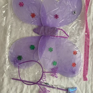 Barn Fjäril Vingar I 3 Delar  - Två diadem i plast, ett lila och ett blått, med fjärilsdetaljer och glittriga blommor. Perfekt för maskerad eller temafest. Matchande vingar och trollspö ingår, allt i lätta syntetmaterial. Färgglada och lekfulla accessoarer som sticker ut.  69kr/paket , samma frakt , 3 år + 
