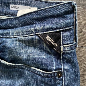 Replay Waitom Regular Fit Jeans 32 - Säljer ett par blå Replay Waitom jeans i regular fit. Klassisk femficksmodell med snygga slitningar och kontrastsömmar. Jeansen har raka ben och coola detaljer på bakfickorna. Perfekta för dig som gillar en avslappnad stil.
