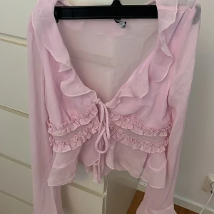Ljusrosa volangblus med knyt - Supersöt ljusrosa blus med volangdetaljer och knyt framtill, flera lager volanger som ger en romantisk vibe. Perfekt för dig som gillar en feminin och trendig stil. Har aldrig använt den!!!