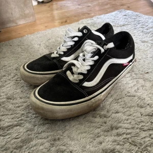 Svarta Vans Old Skool sneakers - Klassiska Vans Old Skool sneakers i svart med vit sula och ikonisk vit sidorand. Skorna har snörning, rund tå och platt gummisula. Ovandelen är i mocka och canvas för en skön och cool streetstil. Perfekta för dig som gillar skate eller vill ha en tidlös look.