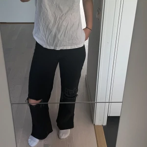 Svarta wide leg jeans med hål - Svarta wide leg jeans från H&M med hög midja och hål på båda knäna. Jeansen är i denim och har klassiska fem fickor. 